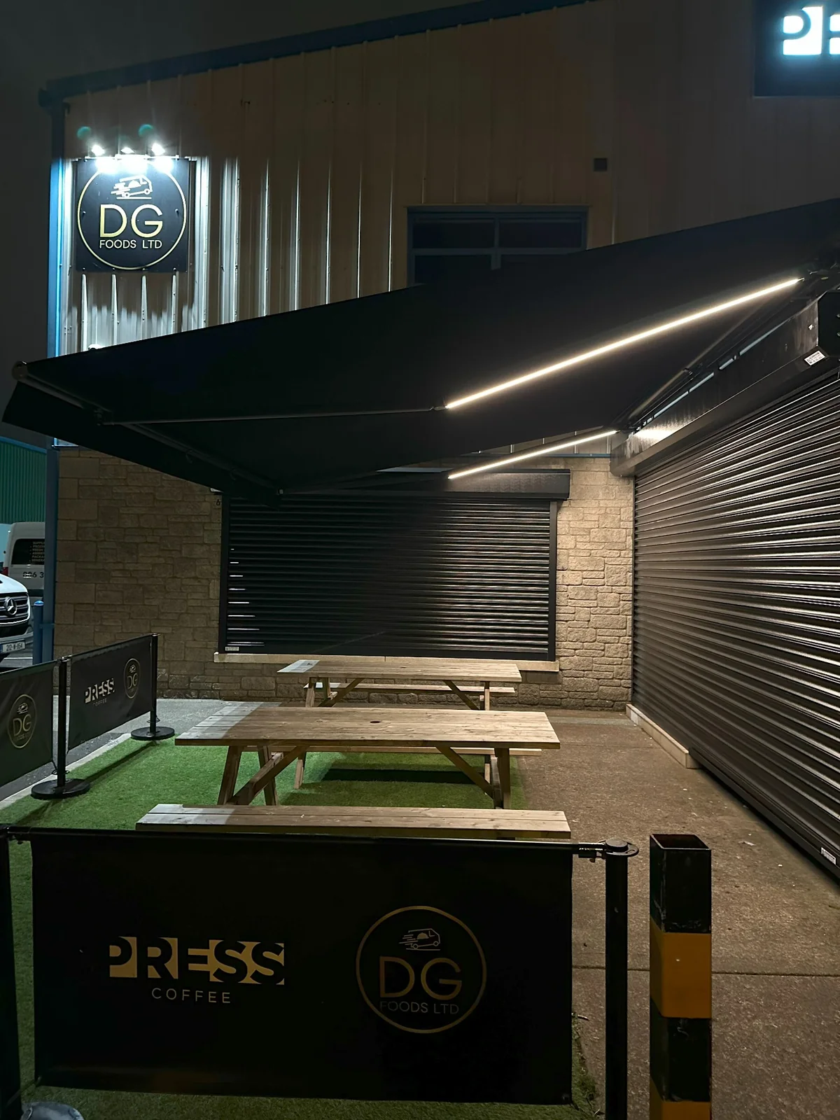 Black commercial awning with bright integrated LED lighting over outdoor tables at night in Waterford