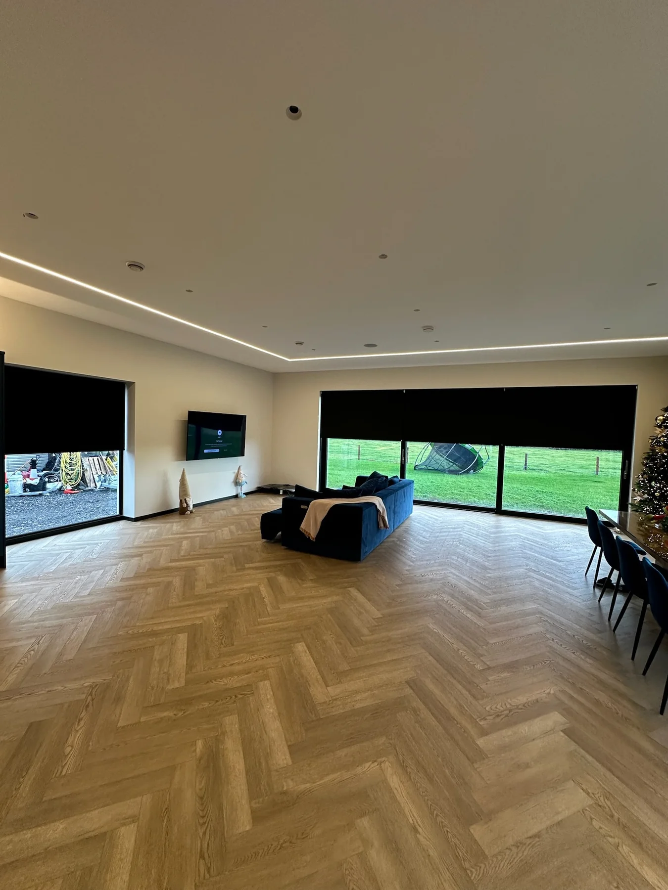 Dark motorised roller blinds covering wide windows in a large open-plan living room