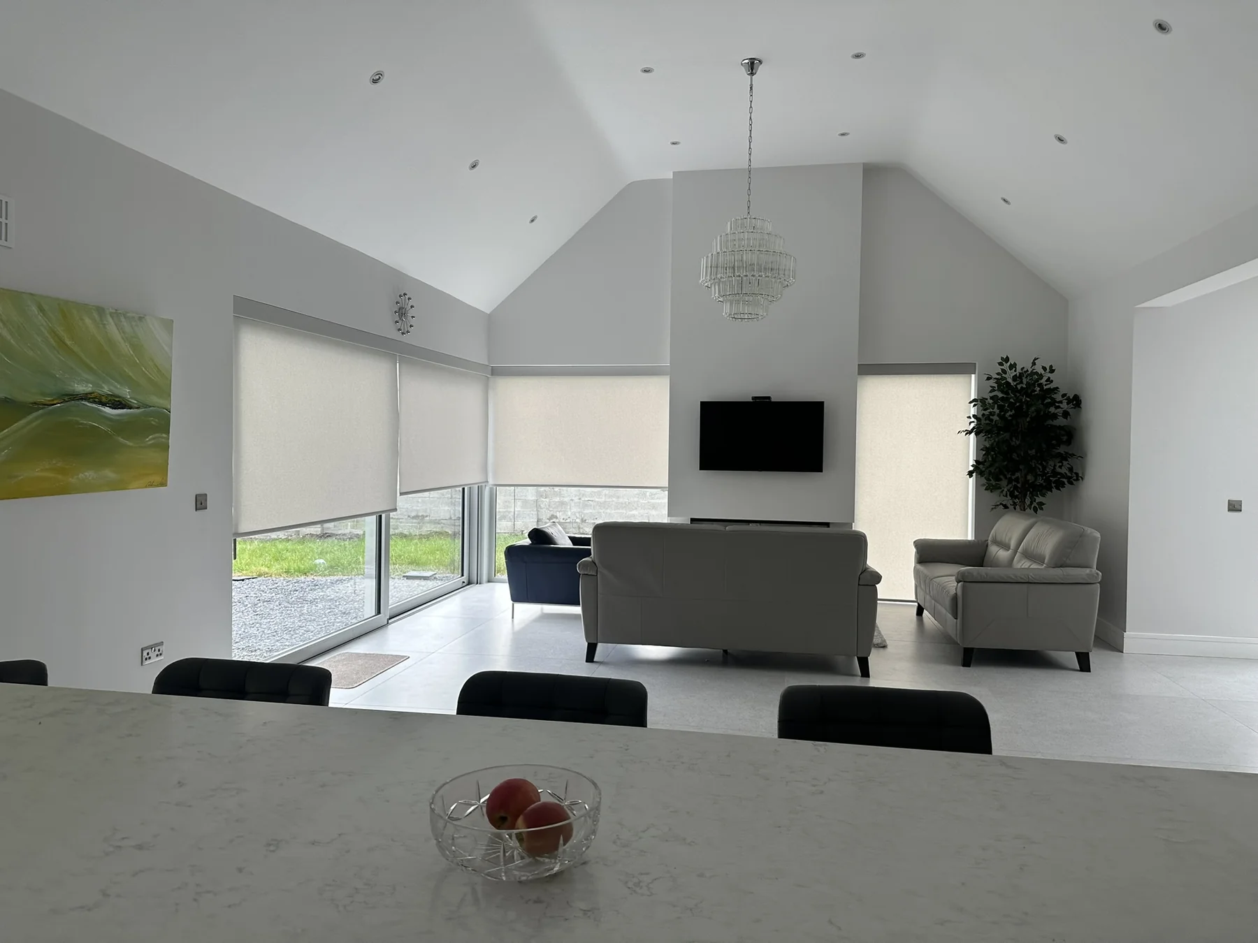 Light motorised roller blinds fitted around a bright open-plan living area
