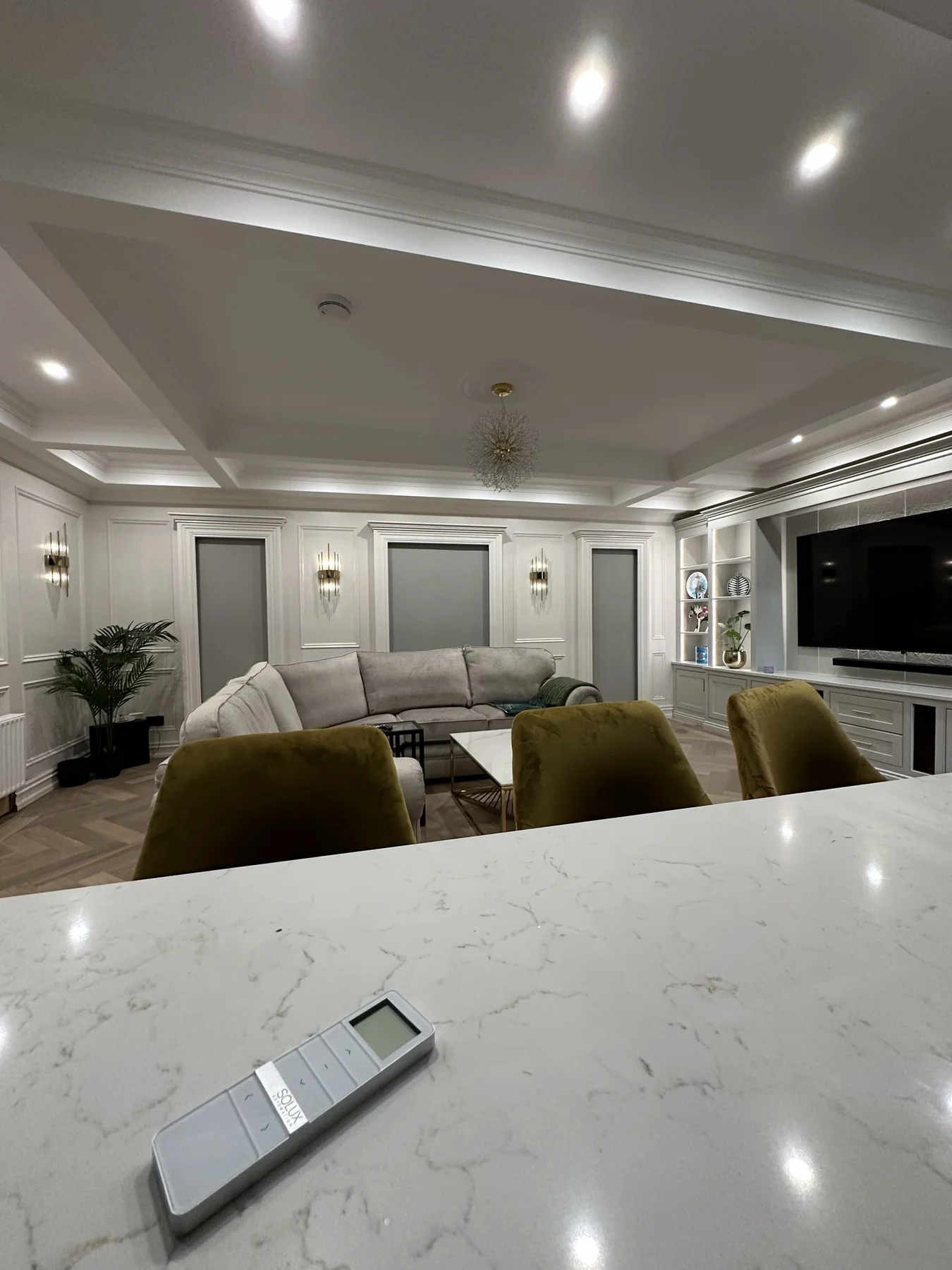 Remote control on a kitchen island overlooking motorised blinds in an open-plan living room
