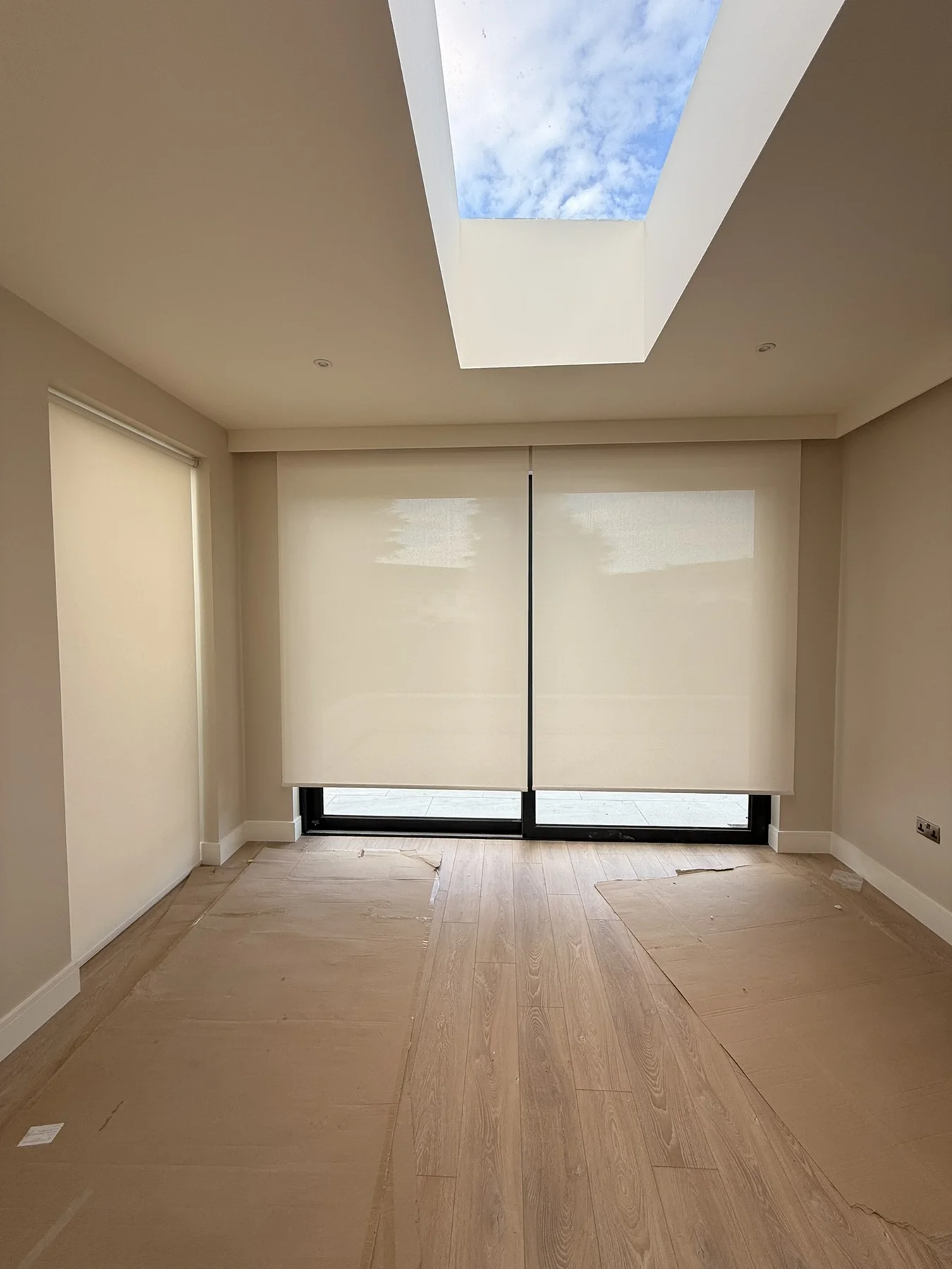 Light motorised roller blinds fitted to wide glazing beneath a rooflight
