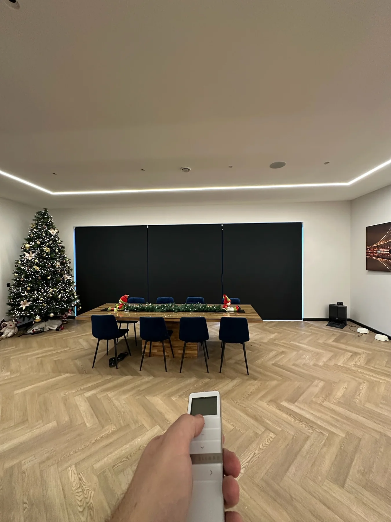 Handheld remote being used to operate dark motorised roller blinds in a large open-plan room