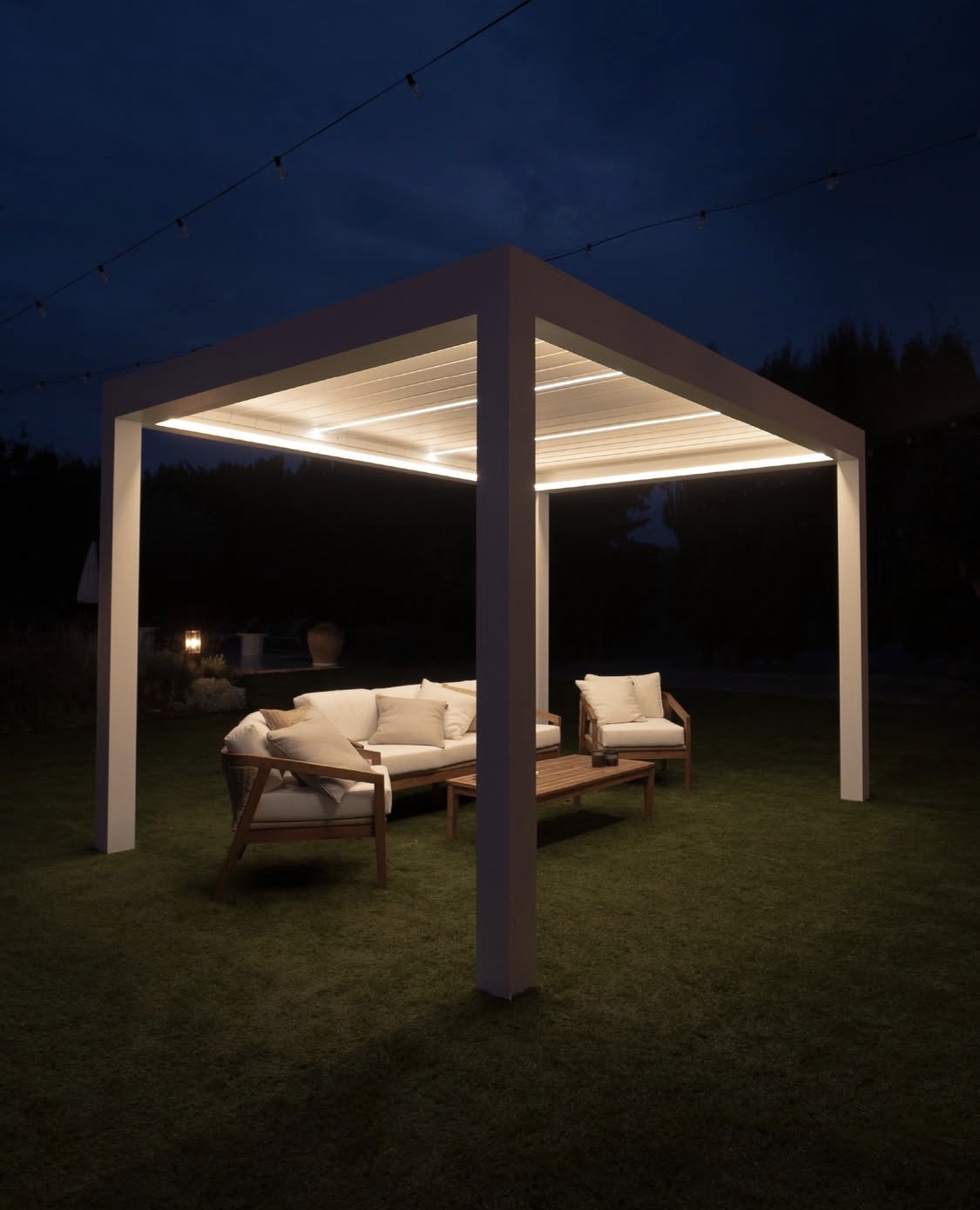 White bioclimatic pergola with integrated evening lighting and lounge furniture beneath the roof