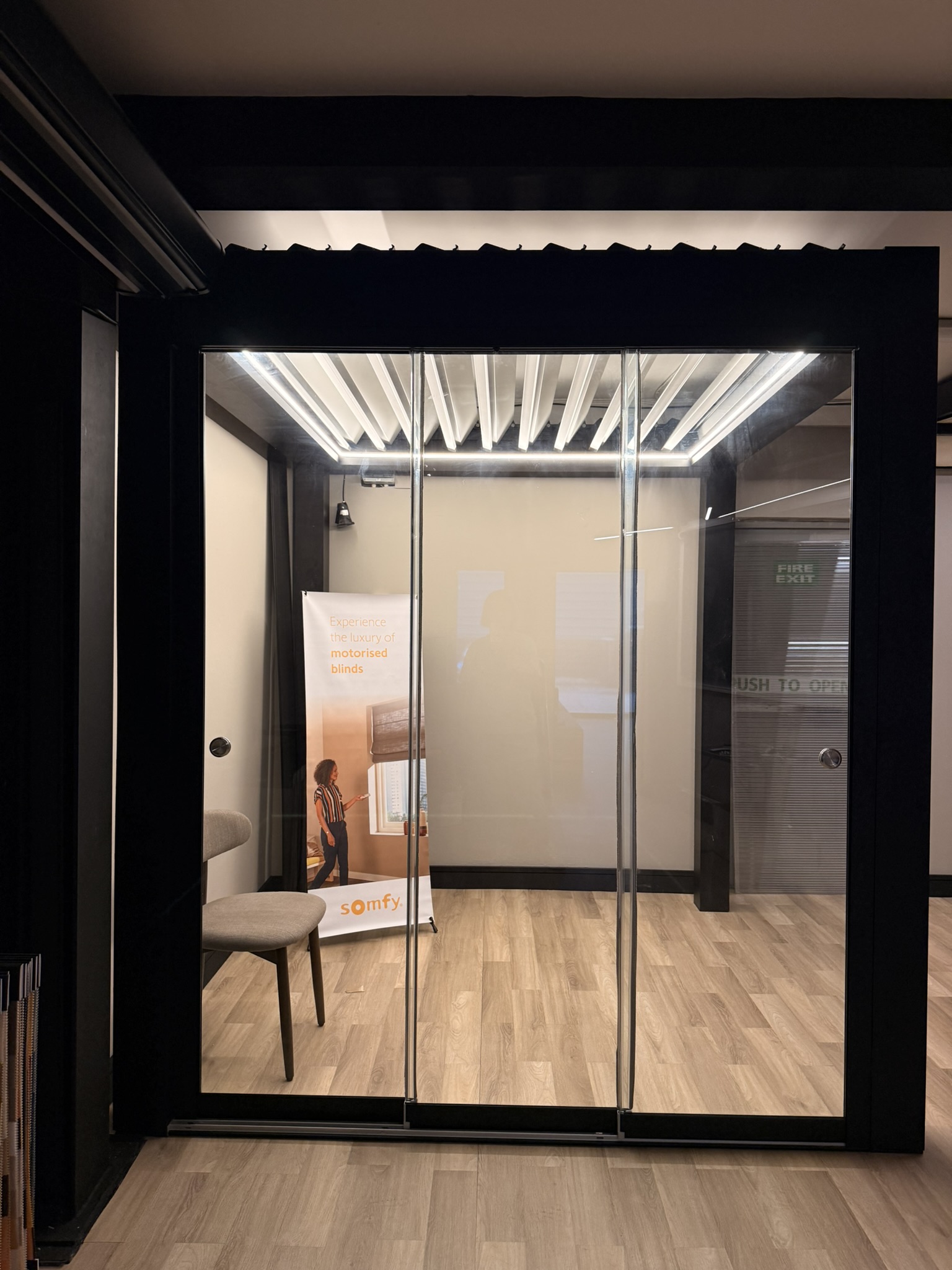 Bioclimatic pergola showroom display with glass sliding panels and illuminated louvred roof