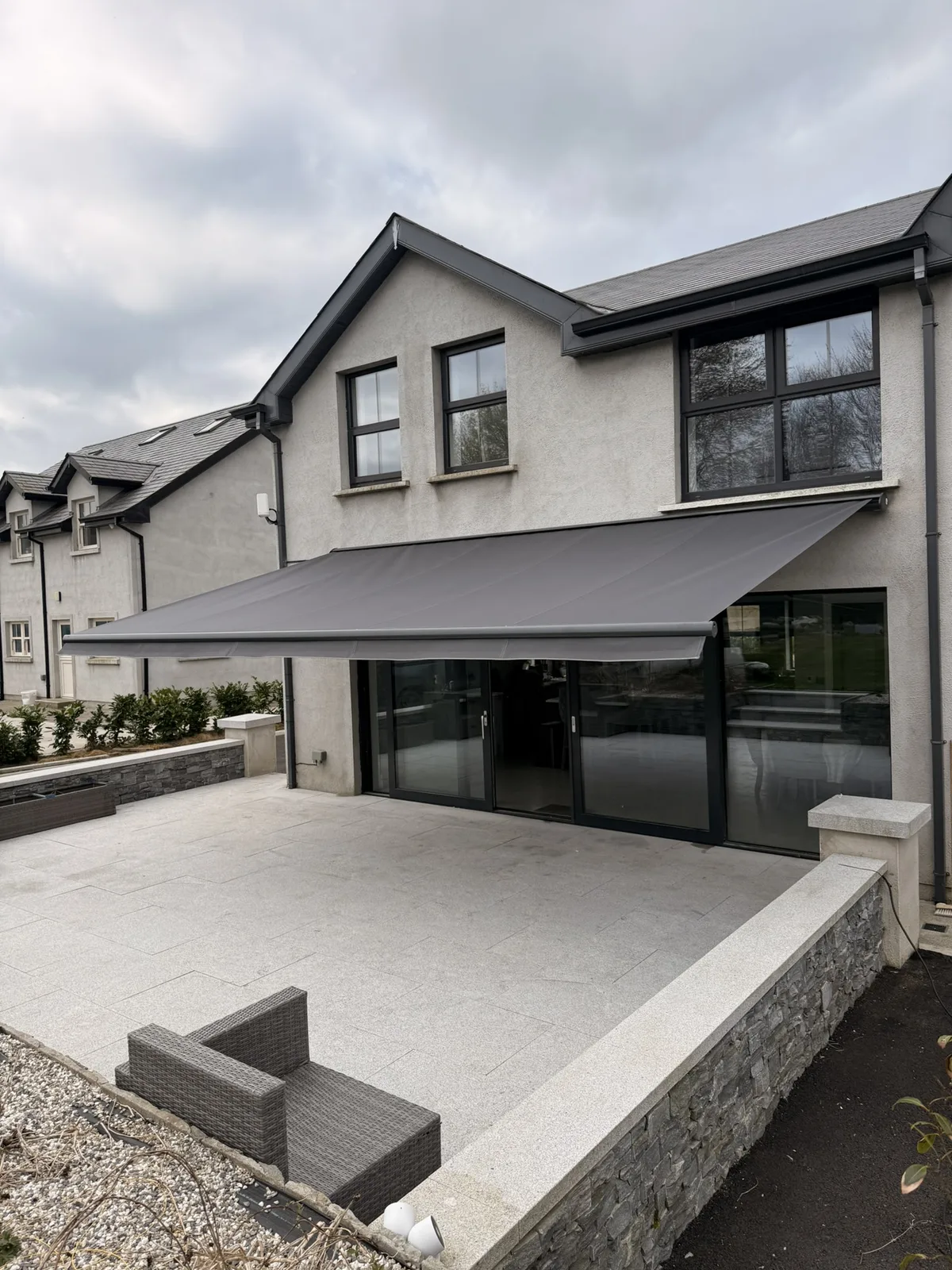 Angled view of a grey semi cassette awning shading a paved patio beside a modern home