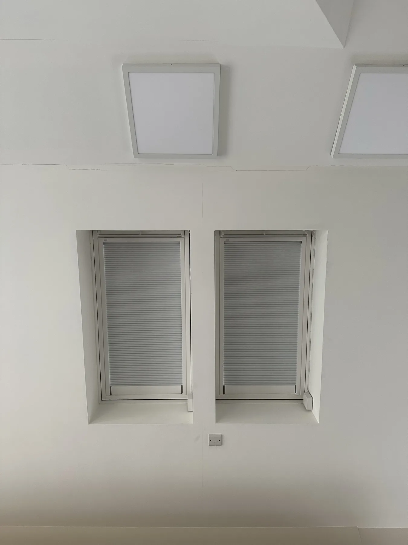 Two pleated blinds fitted to narrow roof windows in a white ceiling