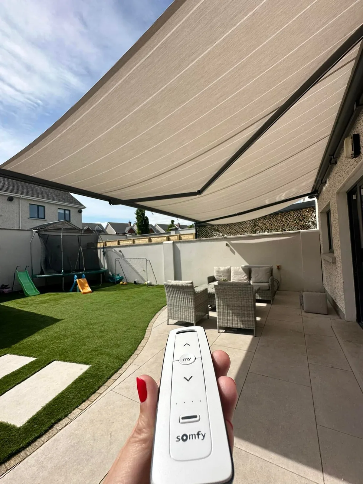 Somfy remote controlling a large motorised awning over a residential garden patio