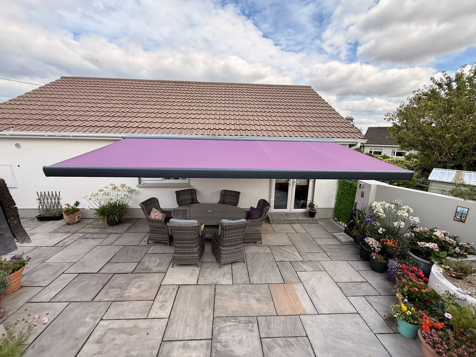 Large retractable awning with purple fabric shading a landscaped patio dining area