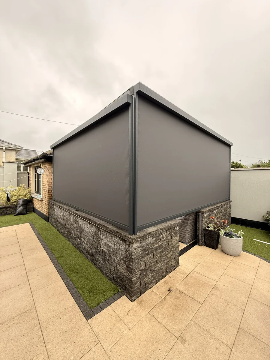Grey ZIP screens enclosing a raised terrace above a stone wall